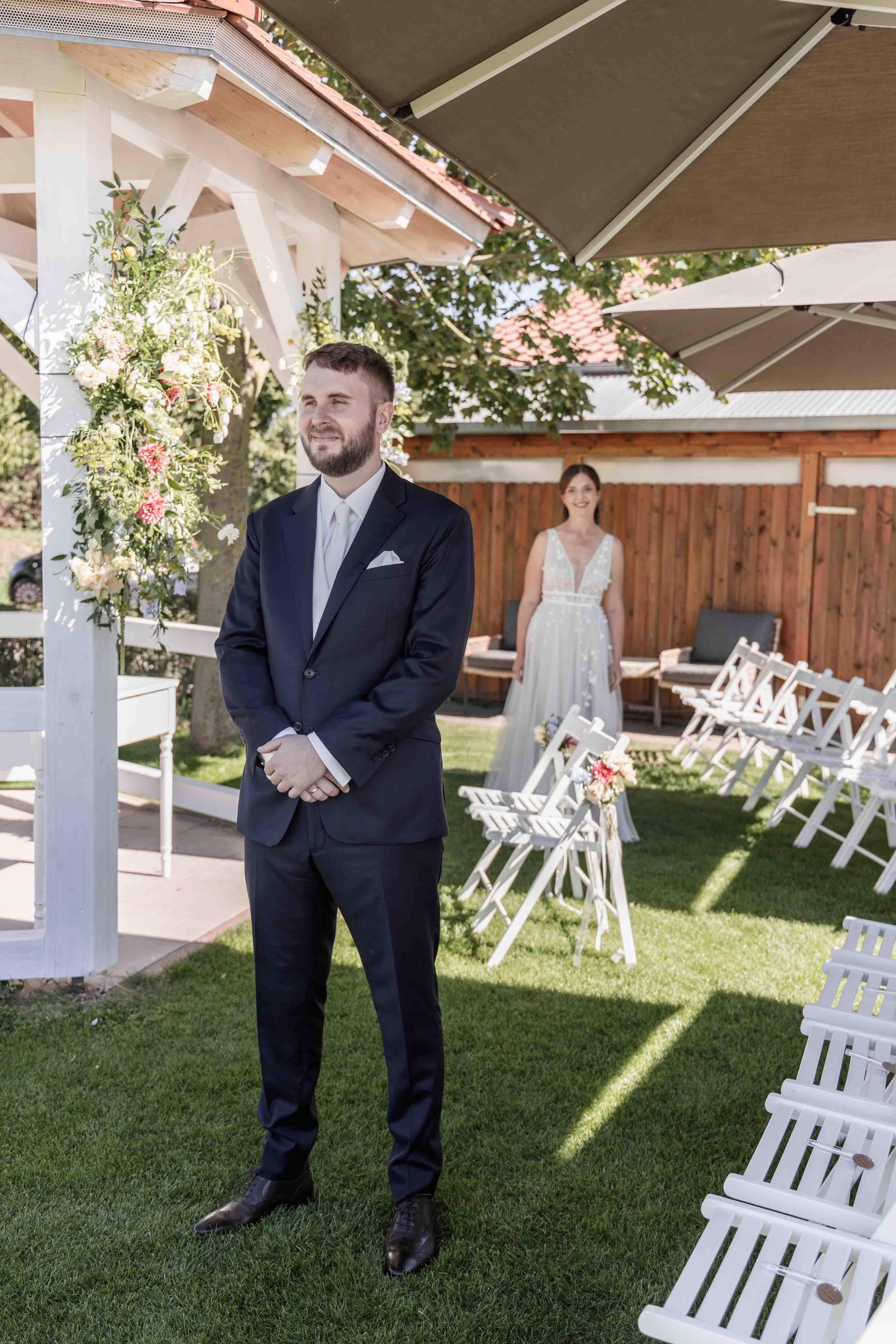 Hochzeitsfoto des Brautpaars - Der Bräutigam ist im Fokus des Bildes, die Braut ist unscharf im Hintergrund zu sehen