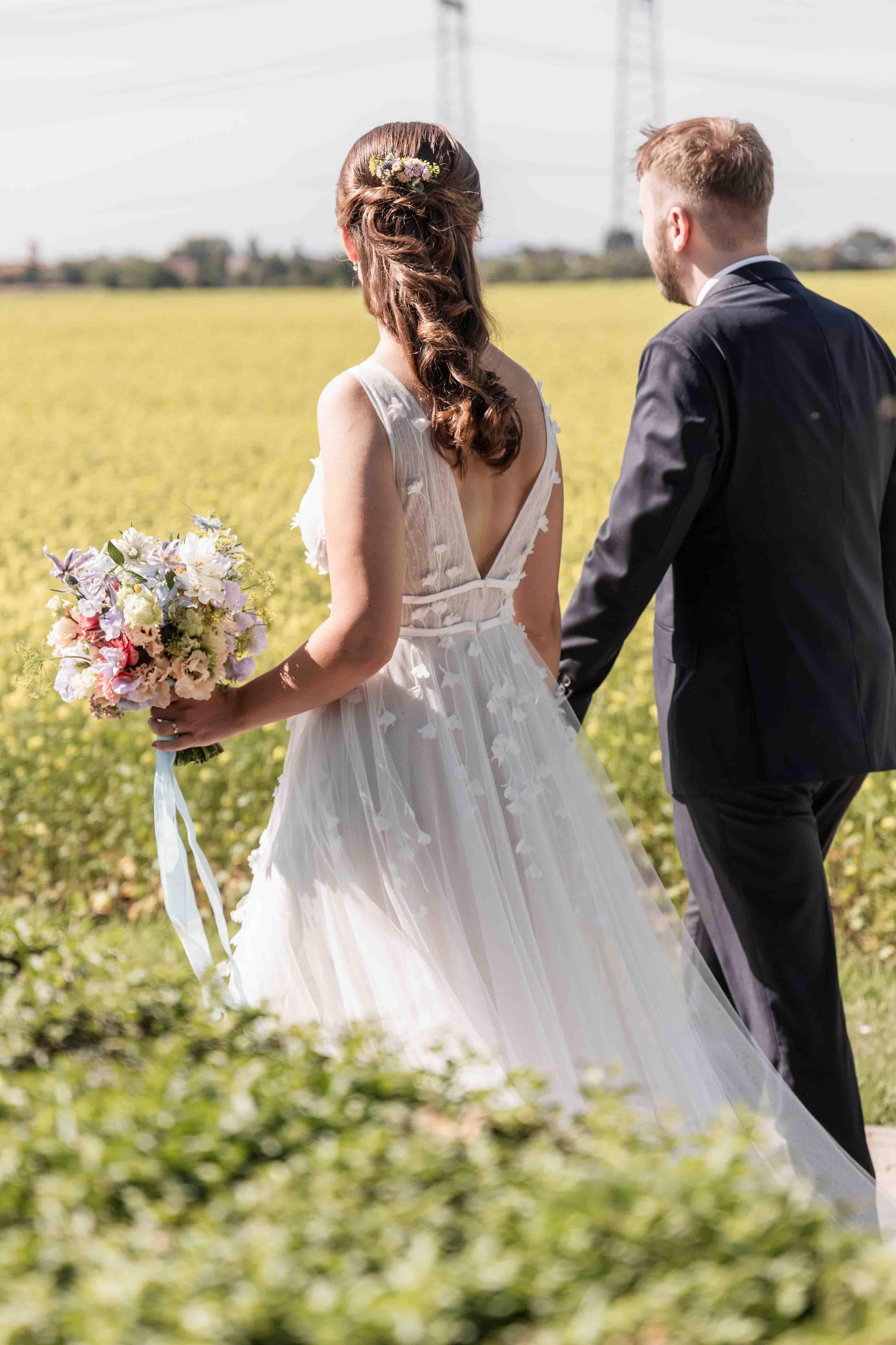 Hochzeitsfoto das Brautpaar läuft zusammen auf einem Weg neben einem Rapsfeld