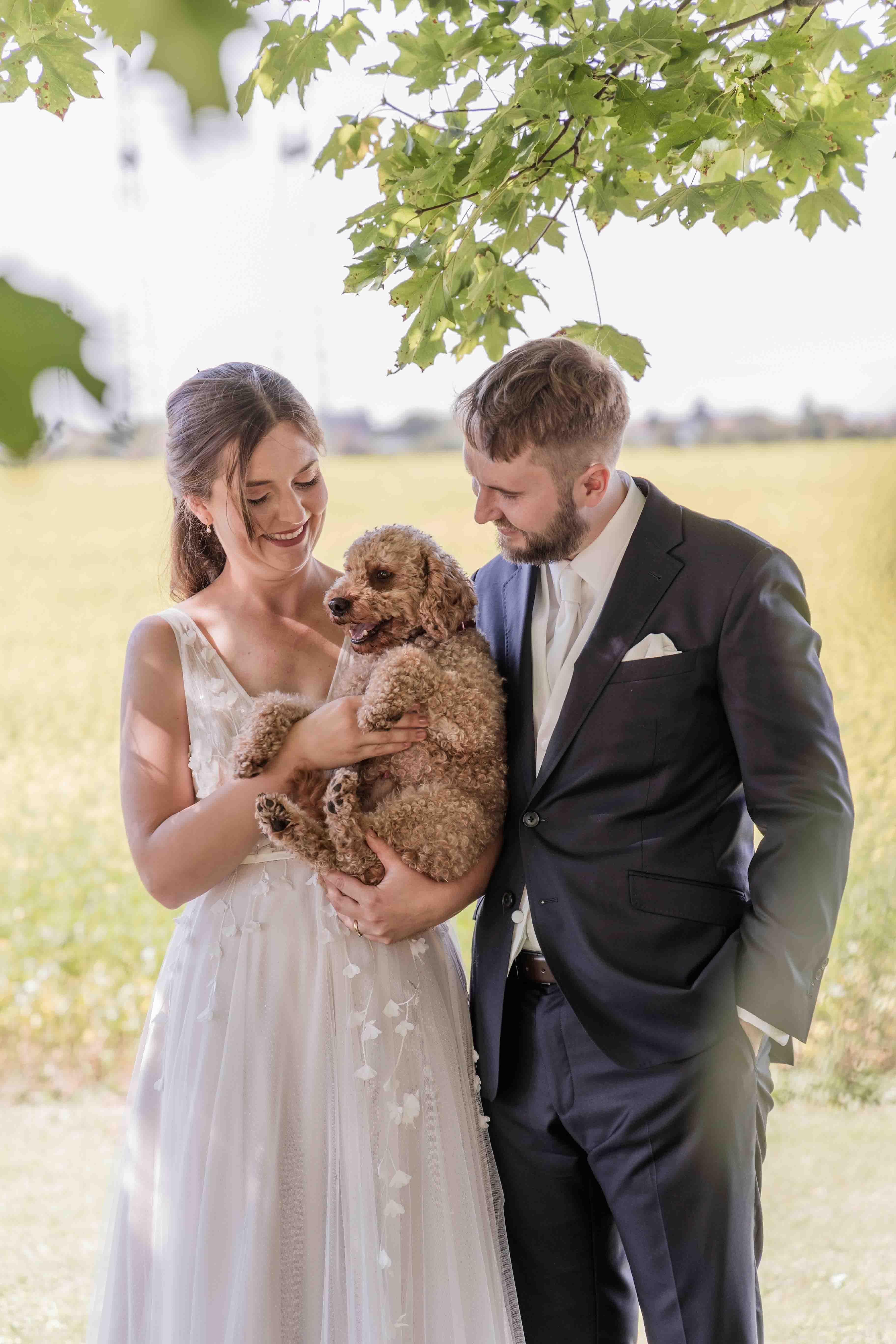Hochzeitsfoto des Brautpaars zusammen mit ihrem Hund im Arm