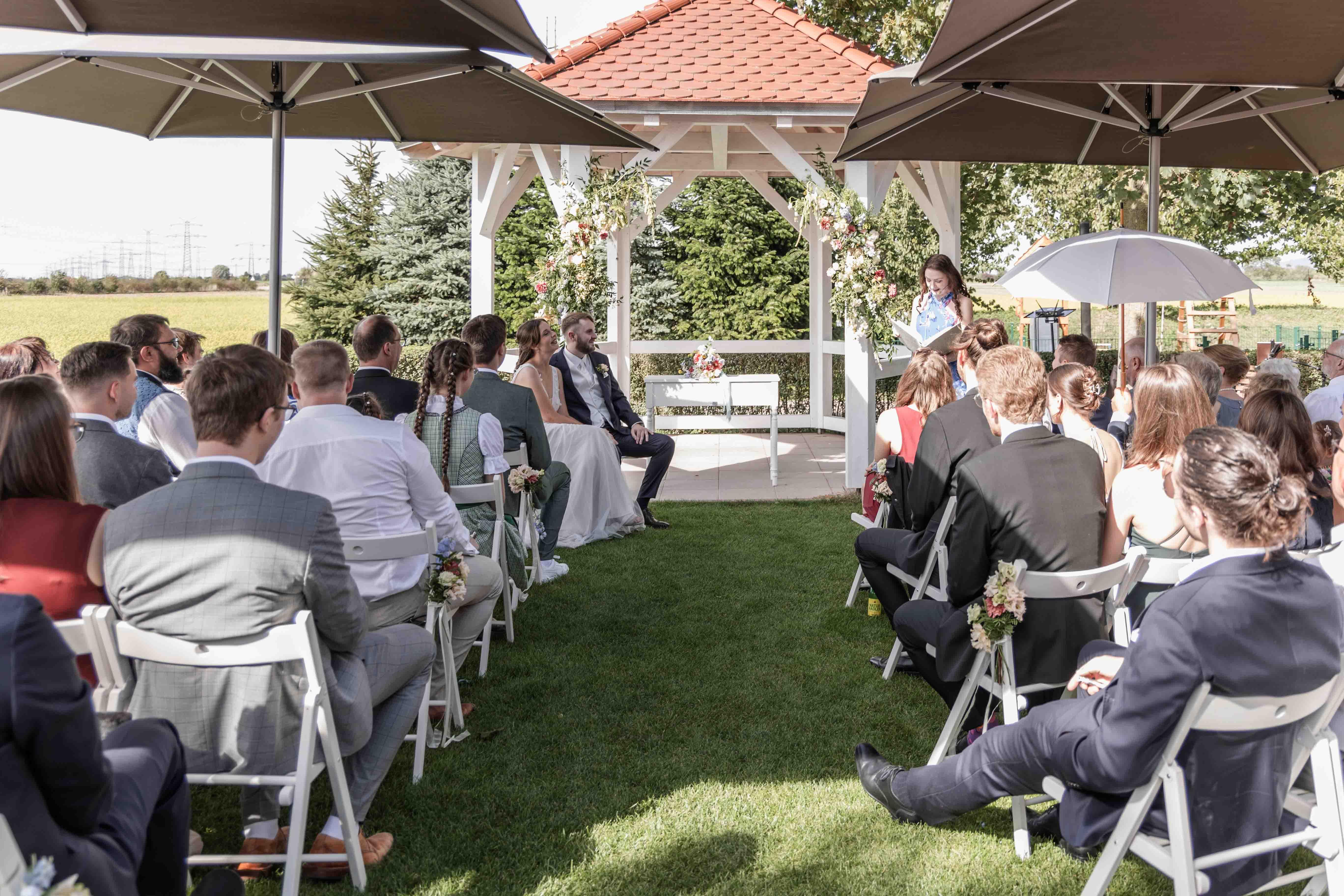 Hochzeitsfoto während der freien Trauung vor dem Gazebo, sowohl Gäste als auch das Brautpaar sind zu sehen