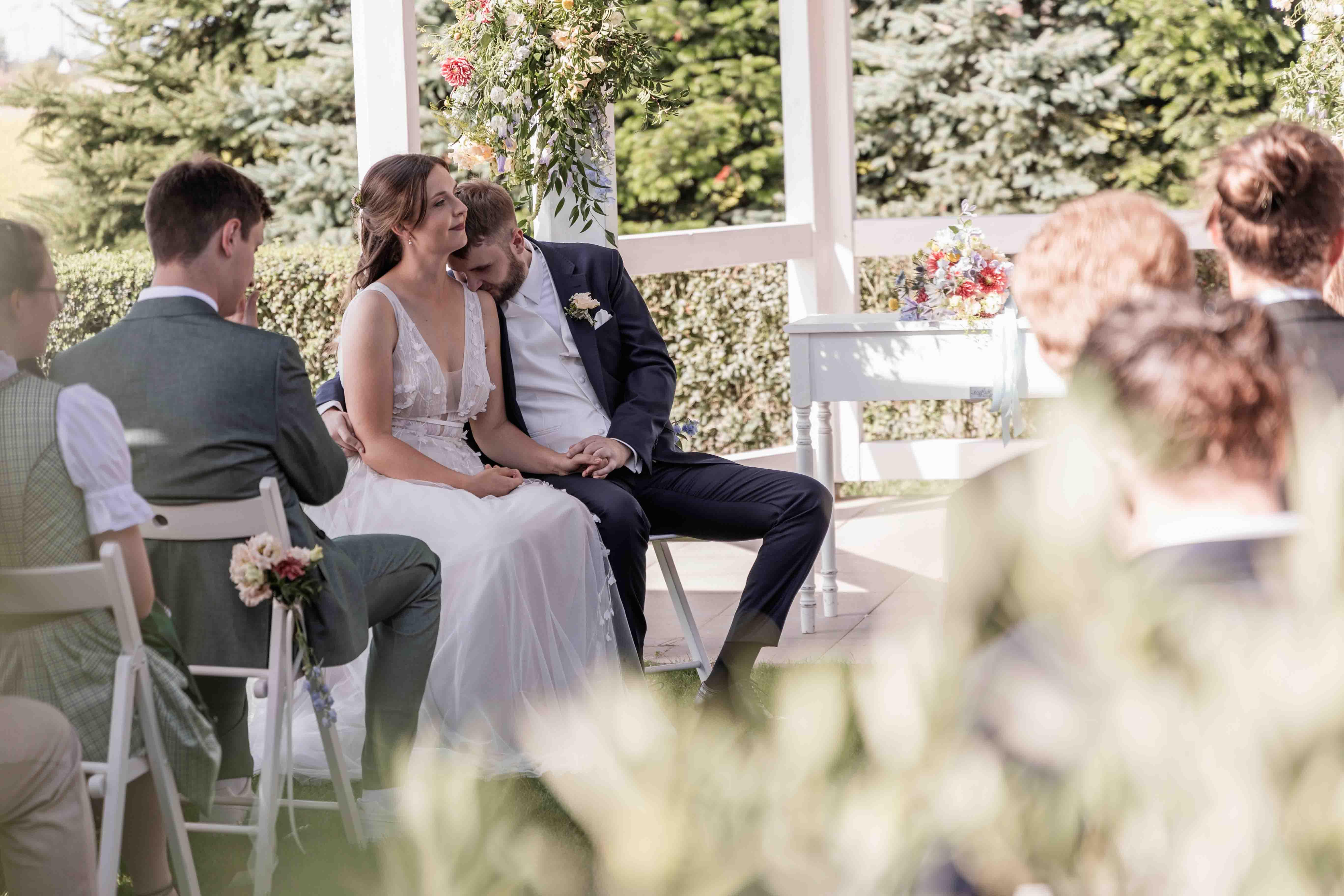 Hochzeitsfoto während der freien Trauung vor dem Gazebo, der Bräutigam küsst die Braut auf die Schulter