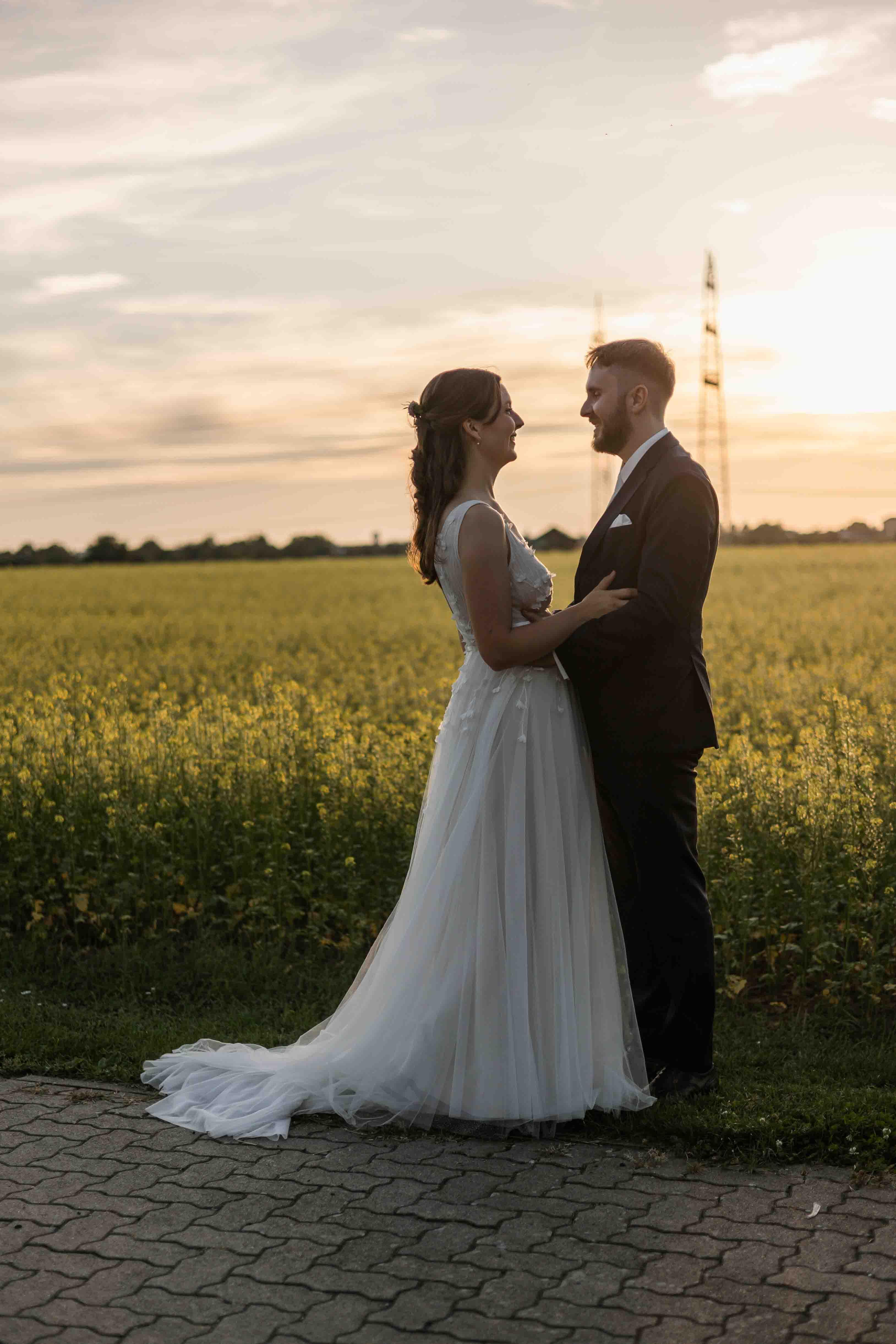 Hochzeitsfoto des Brautpaars bei Sonnenuntergang vor dem Rapsfeld