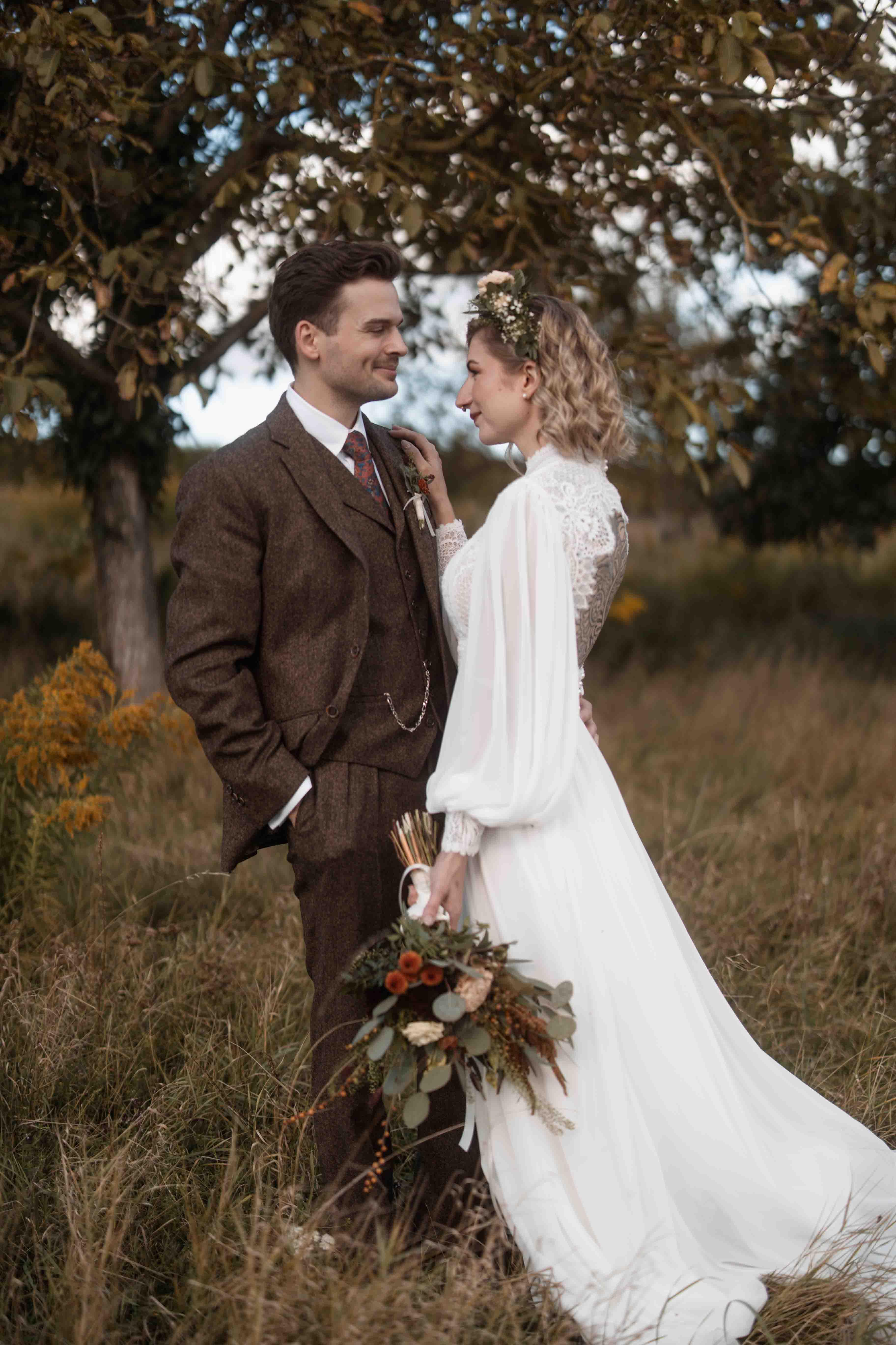 Hochzeitsfoto mit Brautpaar auf einer Wiese neben einem Baum