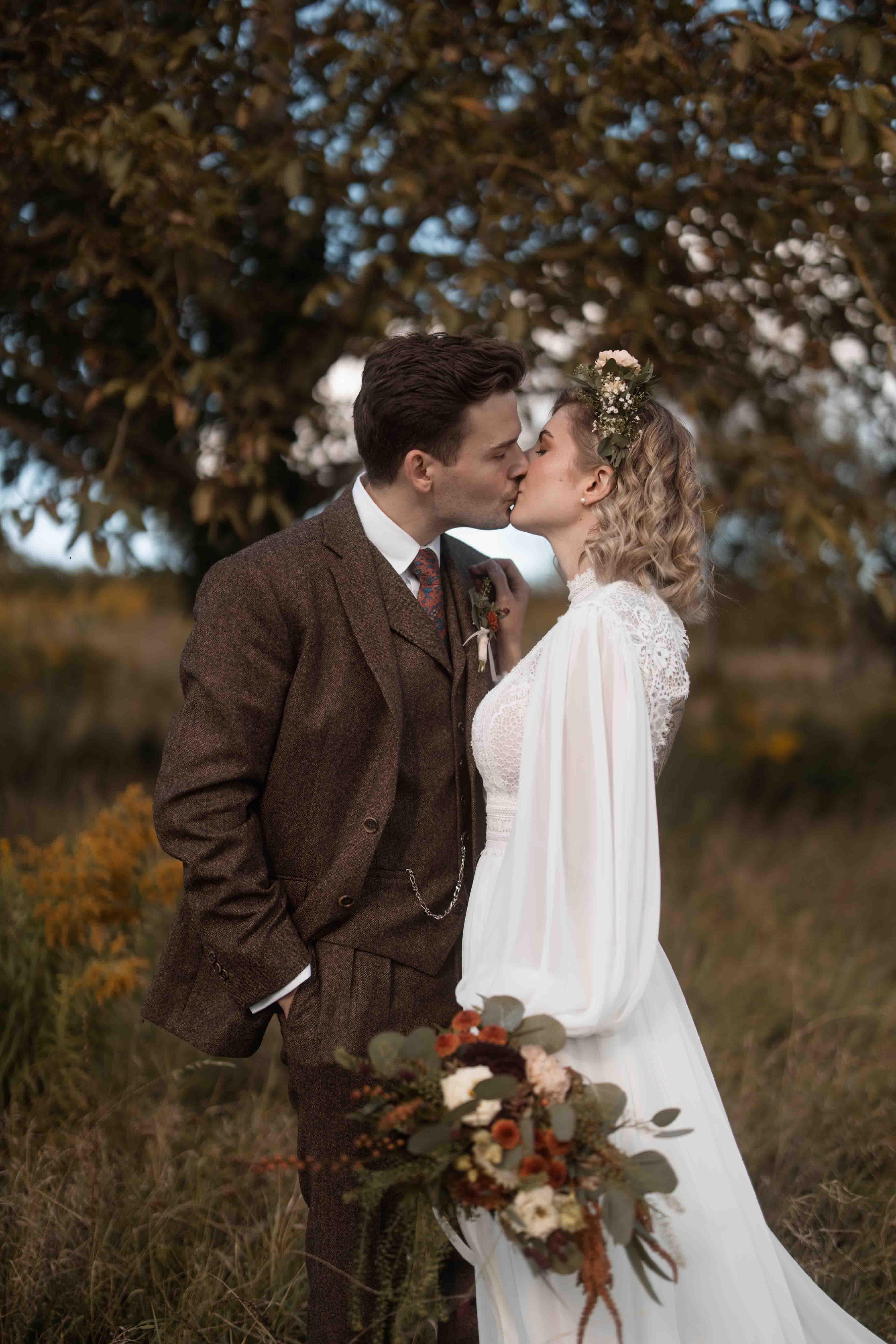 Hochzeitsfoto mit Brautpaar küssend auf einer Wiese neben einem Baum