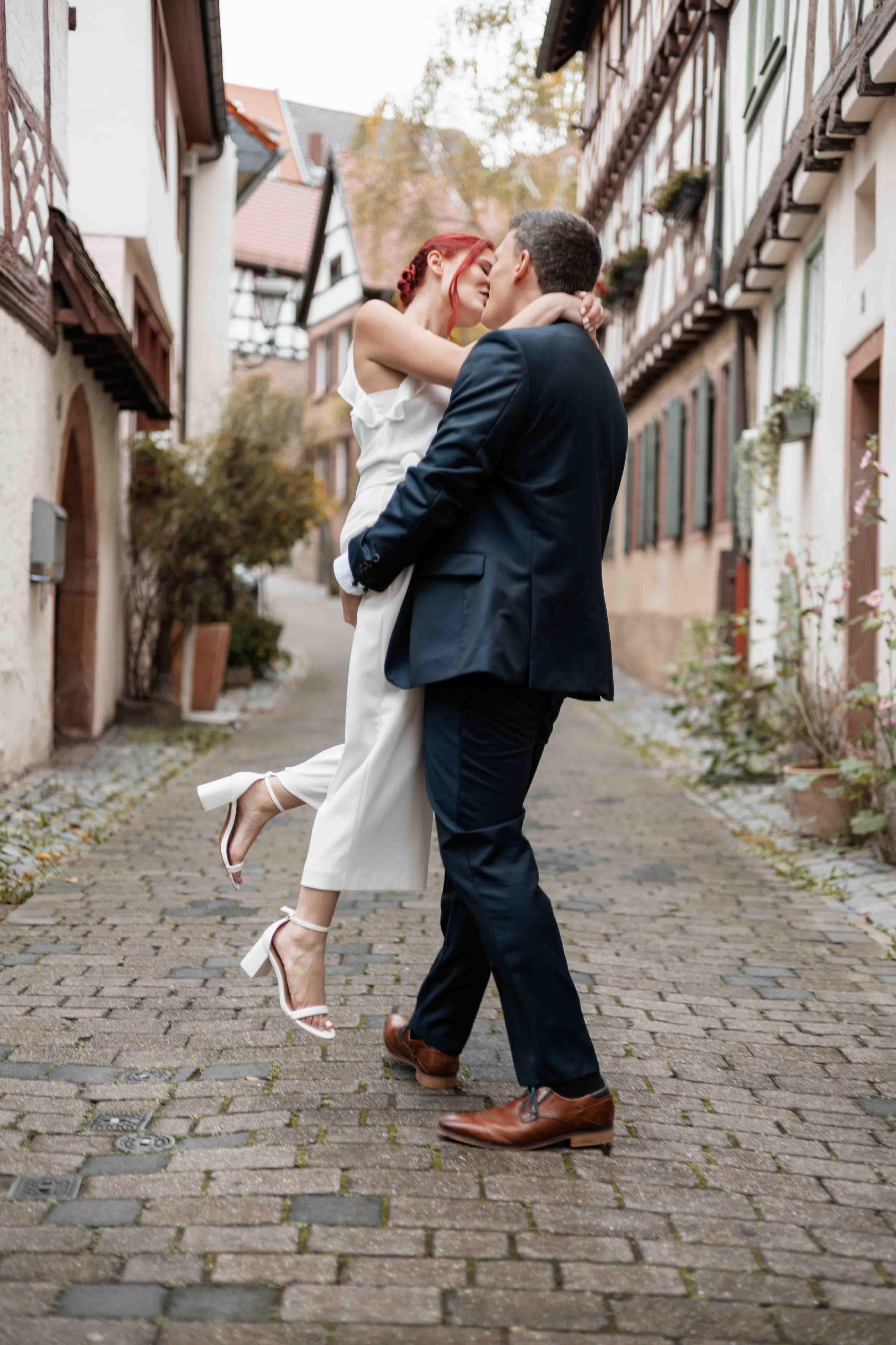 Hochzeitsfoto des Brautpaars küssend auf einer Straße zwischen Fachwerkhäusern