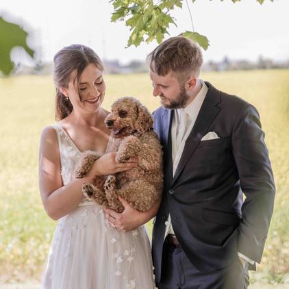Hochzeitsfoto des Brautpaars zusammen mit ihrem Hund im Arm