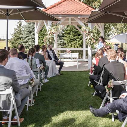 Hochzeitsfoto während der freien Trauung vor dem Gazebo, sowohl Gäste als auch das Brautpaar sind zu sehen