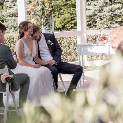 Hochzeitsfoto während der freien Trauung vor dem Gazebo, der Bräutigam küsst die Braut auf die Schulter